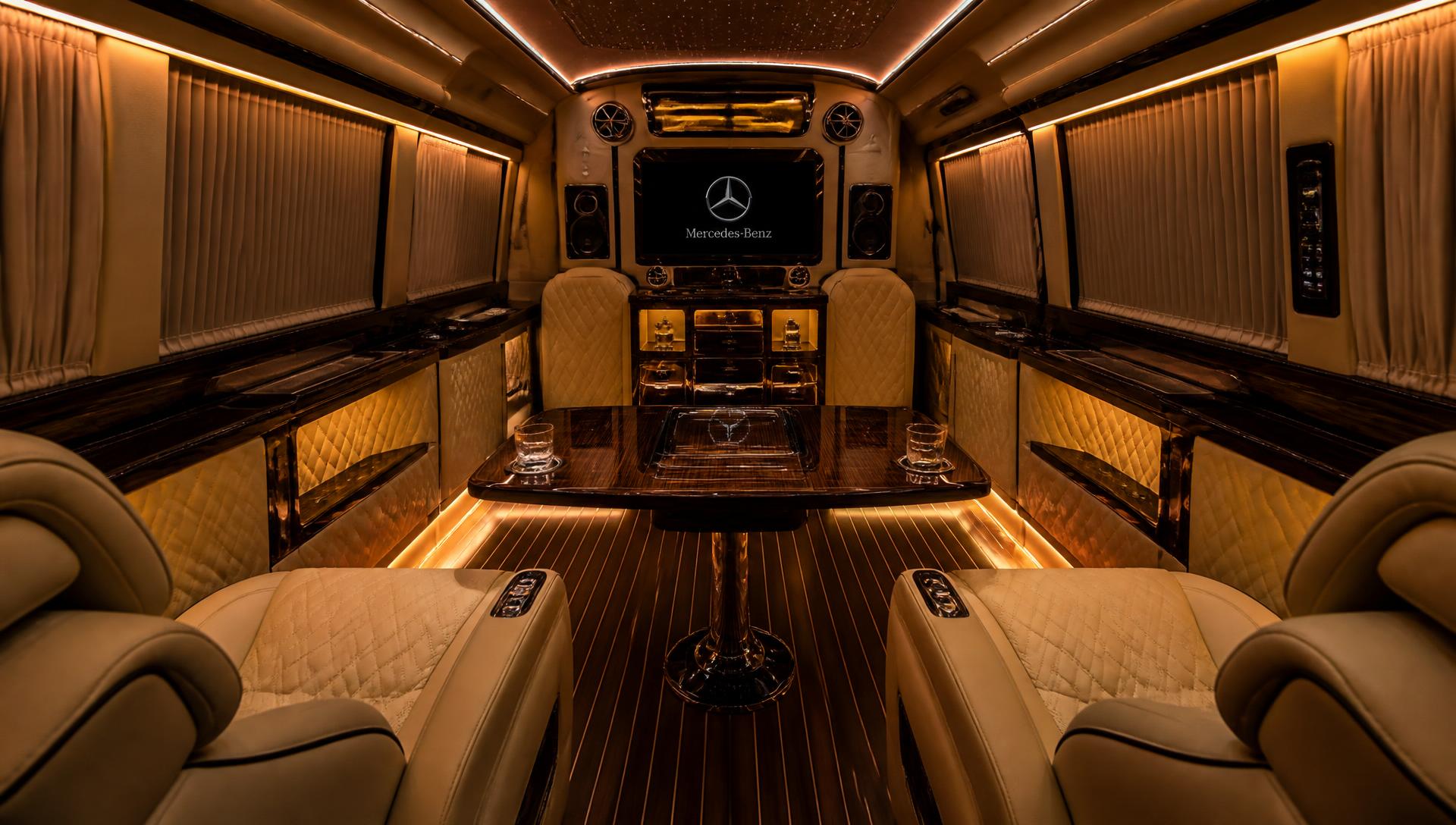 Interior of a Mercedes-Benz VIP jet sprinter with quilted leather captain recliners, a polished walnut conference table and warm ambient lighting